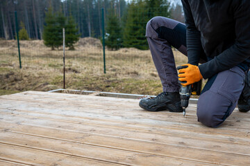 Deck or terrace construction, builder hand with electric screwdriver installing impregnated wooden boards