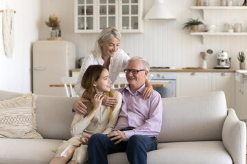 Friendly family have conversation sitting on sofa, senior man relax with mature daughter and adolescent granddaughter in living room, enjoy spending time together. Harmony, relationship, understanding