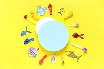 Blank cards with paper fishes, balloons and party whistles on yellow background. April Fools Day celebration