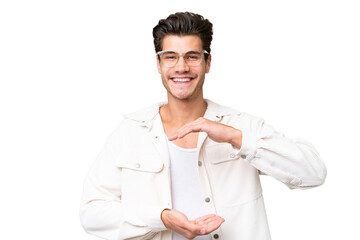 Young handsome caucasian man over isolated background holding copyspace imaginary on the palm to...
