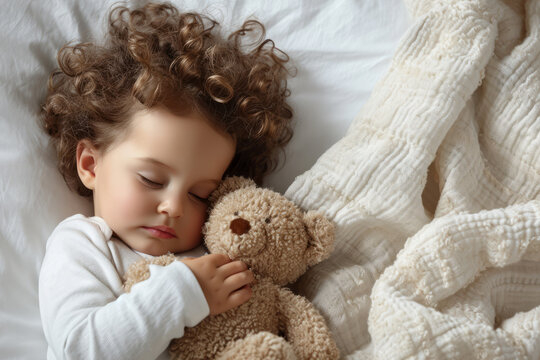Cute little baby girl sleeps in her bed with toy teddy bear. View from above