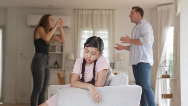 Annoyed and unhappy young girl sitting on sofa trapped in middle of tension by her parent argument in living room. Unhealthy domestic lifestyle and traumatic childhood develop to depression Fastidious