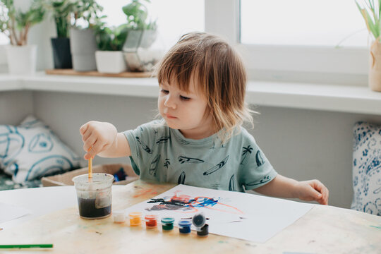 Little girl draws with paints at the kitchen