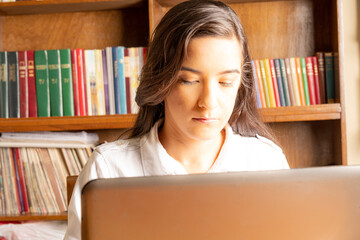 young business woman, concentrated working on a laptop, with a bookcase full of books in the background