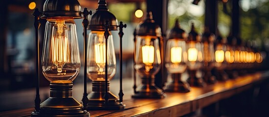 A row of lanterns illuminating a wooden table at an outdoor event. The buildings facade reflected in the glass bottles and barware on display - obrazy, fototapety, plakaty