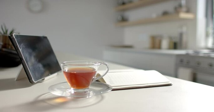 A tablet and a cup of tea rest on a kitchen counter with copy space