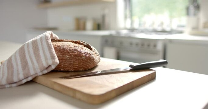 A loaf of bread rests on a cutting board, partially covered by a cloth