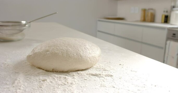 A ball of dough sits on a floured surface in a kitchen at home