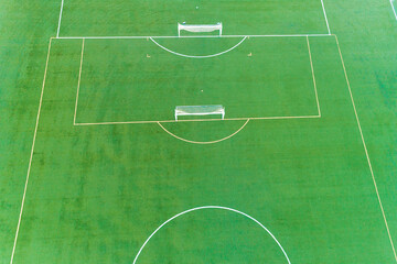 A soccer field with two goals and a bench. The field is green and well maintained. Aerial drone view