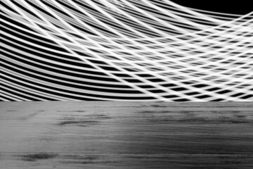 Monochrome photo of abstract light patterns on black background, behind a wooden surface.