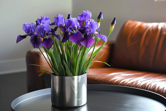 Deep purple irises in a silver vase on a sleek black table by a chestnut leather sofa.