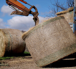 A mechanical rake and fork arm moves and unloads a bale of hay from a truck - 760101208
