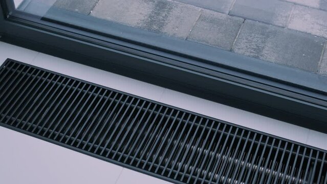 An up-close view of a modern, clean-lined HVAC floor register near a window, blending seamlessly with the sleek interior design