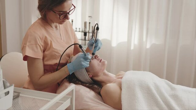 A skilled beautician provides a rejuvenating microcurrent facial therapy to a relaxed female client in a serene salon setting.