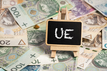 Black writing board on a wooden frame with the inscription "UE", Polish zloty PLN banknotes scattered in the background (selective focus) 