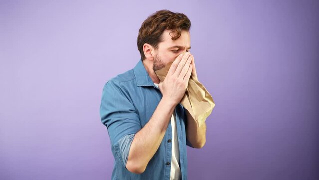 Man in a studio having a panic attack and using a paper bag to breathe and calm down