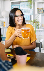 Happy young woman holding beer enjoying brunch with friends at bar. Food and drink concept.