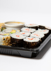 Close up of sushi to go in a black takeaway box with wooden chopsticks on white background