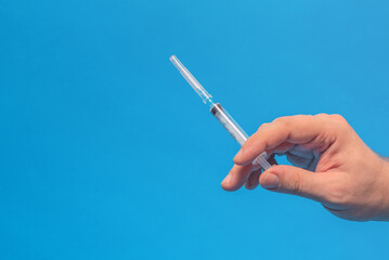 A man holds a medical disposable syringe in his hand, on a blue background