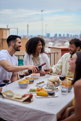 Vertical young smiling Caucasian man serving red wine to guests at food table in celebration with...