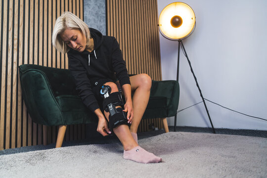 young woman adjusting the angle of knee brace support for leg or knee injury at home, healthcare concept. High quality photo