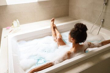 Woman bathes in foamfilled bathtub, relaxing in bathroom fixture