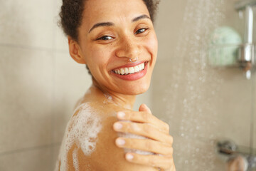 A woman happily showers, smiling as she washes her face, hair, and body