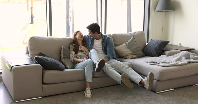 Happy married couple flopped down on sofa in living room, spend carefree weekend leisure together in modern living room, enjoy talk, dating and time together. Tenancy, new property renters, relaxation