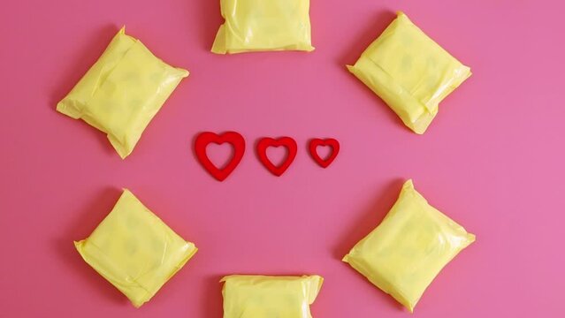 Yellow feminine pads and three red hearts on pink.