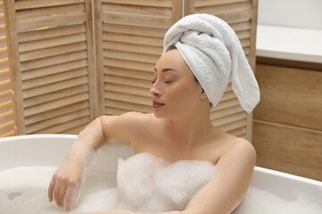 Beautiful woman taking bath with foam in tub indoors