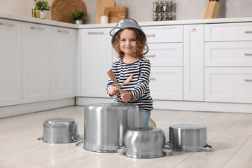 Little girl pretending to play drums on pots in kitchen