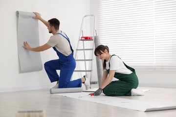 Woman applying glue onto wallpaper while man hanging sheet indoors - obrazy, fototapety, plakaty