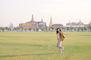 Traveler asian woman in her 30s, backpack slung over her shoulder, explores Wat Pra Kaew with...
