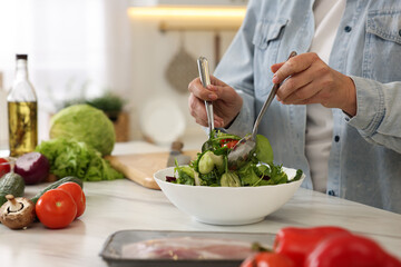 Woman making salad at white marble table in kitchen, closeup