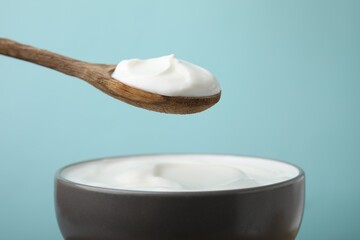 Eating delicious natural yogurt on light blue background, closeup