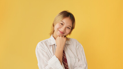 Smiling young woman dressed in shirt and tie looking at camera isolated on yellow background in studio