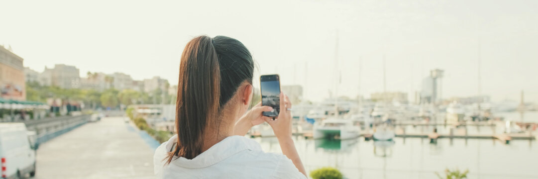 Young woman taking photo of the sea port on mobile phone. Back view, Panorama
