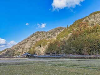 田舎の山間部で遠くに鉄道の駅が見える田んぼと山の広がる風景