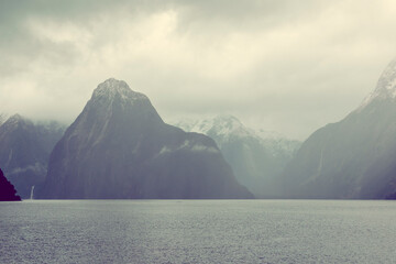 Photograph of mountains in clouds and mist viewed from the water in Milford Sound in Fiordland...