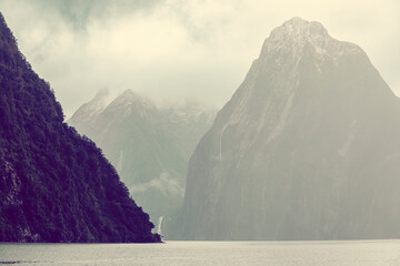 Photograph of mountains in clouds and mist viewed from the water in Milford Sound in Fiordland...