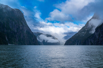 Photograph of mountains in clouds and mist viewed from the water in Milford Sound in Fiordland...