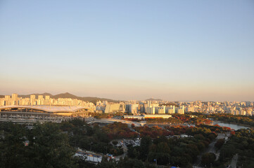 SEOUL, SOUTH KOREA - OCTOBER 24, 2022: Colourful foliage trees in Autumn with Han river, World Cup stadium, and skyscraper buildings in the afternoon and blue sky.