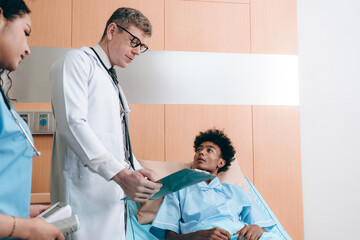 Obraz premium Doctor and African American patient talking in hospital ward about diagnosis and treatment for teenager in bed. Black specialist man with stethoscope consulting sick young adult