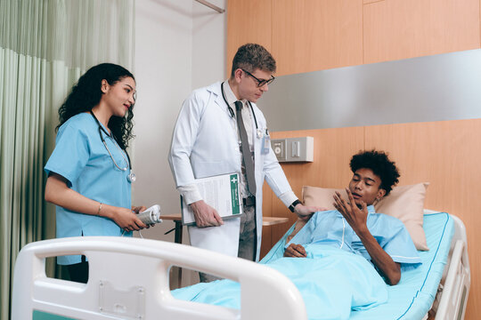 Doctor and African American patient talking in hospital ward about diagnosis and treatment for teenager in bed. Black specialist man with stethoscope consulting sick young adult