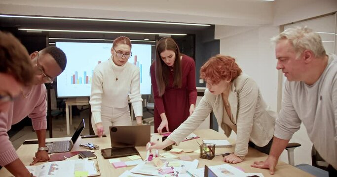 A multicultural group of people engages in a team meeting, discussing reports and analytics with laptops and documents on the table, their collaborative efforts aimed at achieving common objectives.