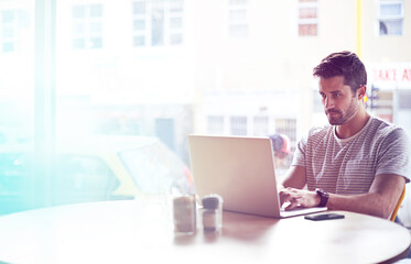 Young man, cafe and typing with laptop for communication, social media or networking at indoor restaurant. Male person, freelancer or remote work on computer for research or reading at coffee shop