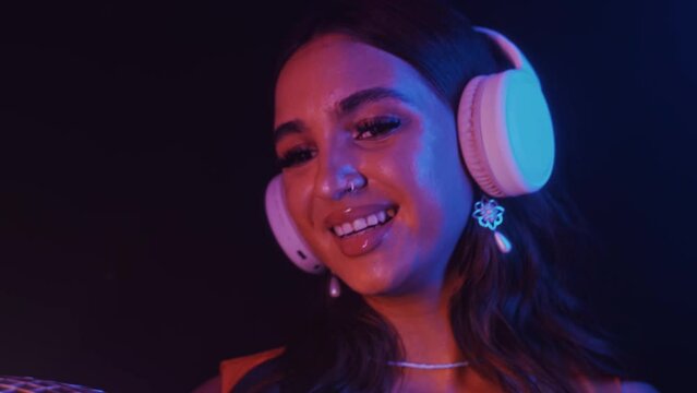 Tilt up shot of young female DJ in headphones holding disco ball while dancing in nightclub in neon light