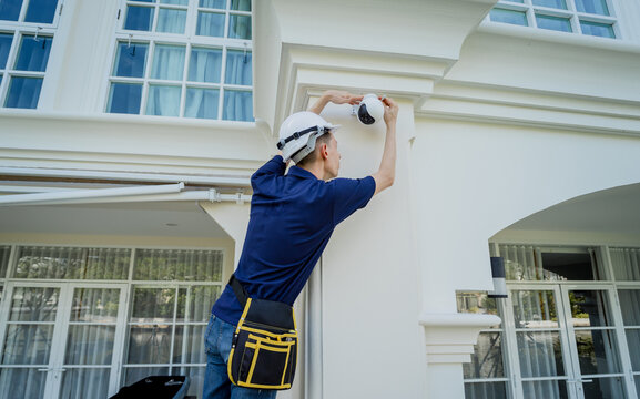 A technician installs a CCTV camera on the facade of a residential building.