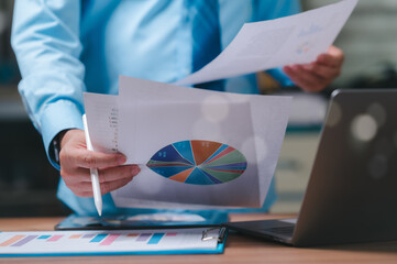 A businessman is holding a pen and a stack of papers with pie charts on them. He is likely working...