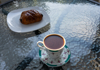Armenian - Turkish coffee from traditional coffee pot jazzve - cezve and a French chocolate croissant on a patio table during sunset